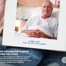 Ein Inserat von FRAGILE Suisse. Eine Person hat ein offenes Tagebuch auf den Knien, darin ein Foto eines älteren Mannes im Bett, der in die Kamera lächelt. Daruntre steht: 18. März 2019: Mein zweites erste Lächeln.