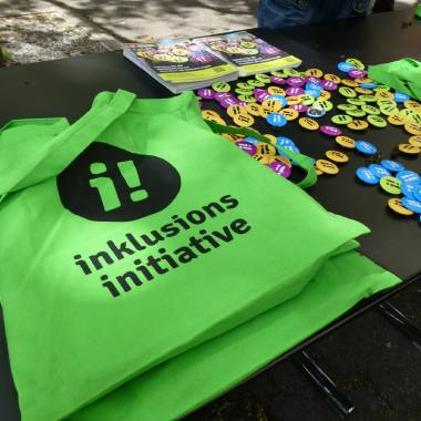 Grüne Taschen und viele Farbige Pins mit dem Logo der Inklusions-Initiative