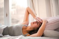 Une femme allongée sur un lit se tient la tête