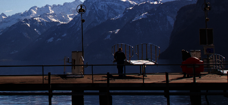 Ein Steg über einem See mit schneebedeckten Bergen im Hintergrund. Auf dem Steg stehen Brücken bereit, die das betreten eines Schiffs erlauben.