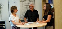 Drei Personen im Gespräch an einem Stehtisch.