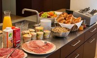 Brunchbuffet mit einer Auswahl an Brot, Zopf, Gipfeli, Aufschnitt, Joghurt, Müesli, frischen Früchten und Orangensaft, angerichtet auf einer Küchentheke.