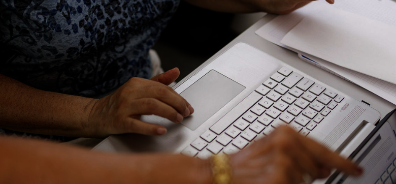 Eine Hand bedient das Mausfeld eines Laptops. Die Hand einer anderen Person zeigt auf den Bildschirm.