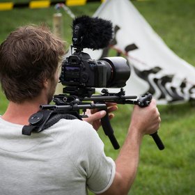 Un homme porte une caméra sur son épaule droite pour filmer