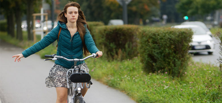 [Bitte in "Französich" uebersetzen:] Eine Frau auf dem Velo. Ihr rechter Arm ist zur Seite ausgestreckt.