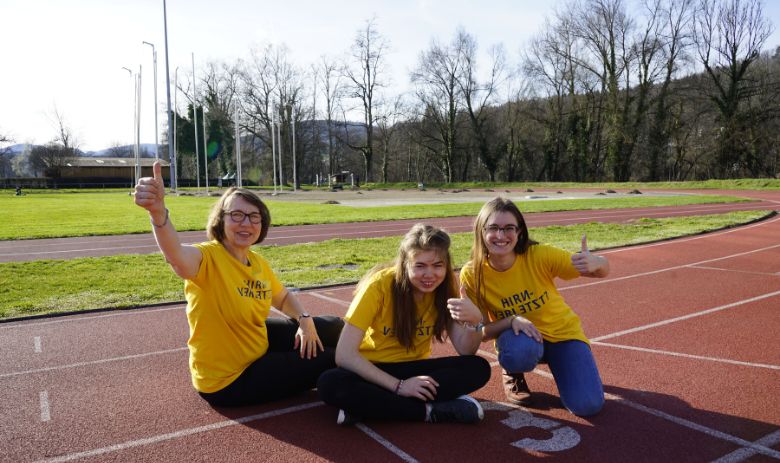 Drei Frauen mit gelben T-Shirts sitzen auf der Laufbahn.