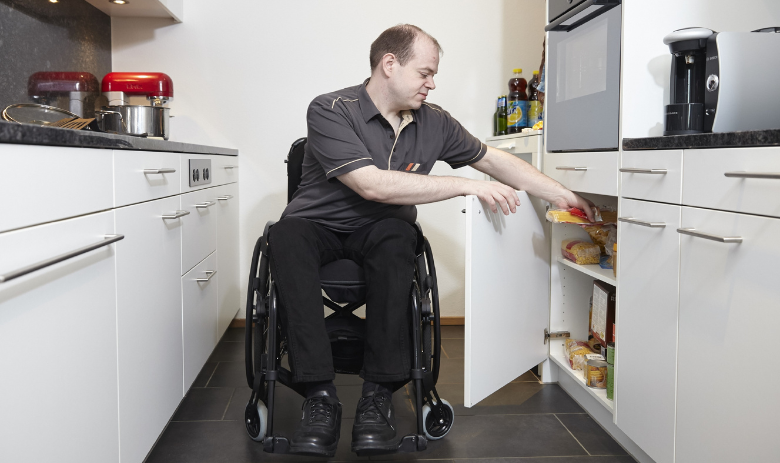 Ein Mann im Rollstuhl in seiner Küche. 