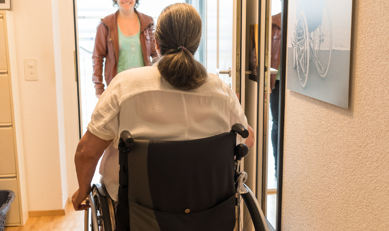 Une femme en fauteuil roulant à la porte d'entrée de son appartement. Une femme attend dehors.