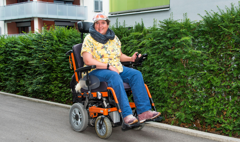 Eine Frau fährt mit dem Elektro-Rollstuhl auf der Strasse.